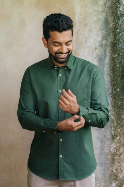 Man in green shirt adjusting cuff, smiling