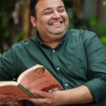 Man smiling and reading book in green shirt