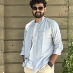 Man in light blue shirt and sunglasses posing against a stone wall.