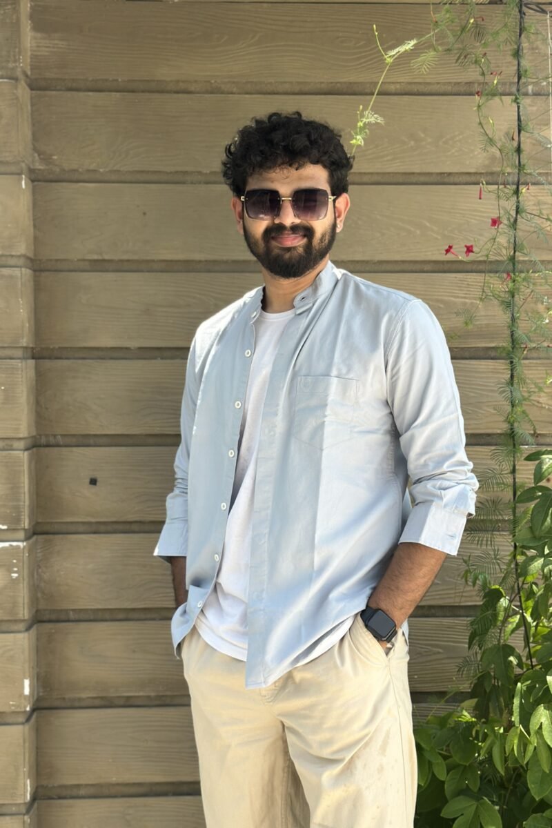 Man in light blue shirt and sunglasses posing against a stone wall.