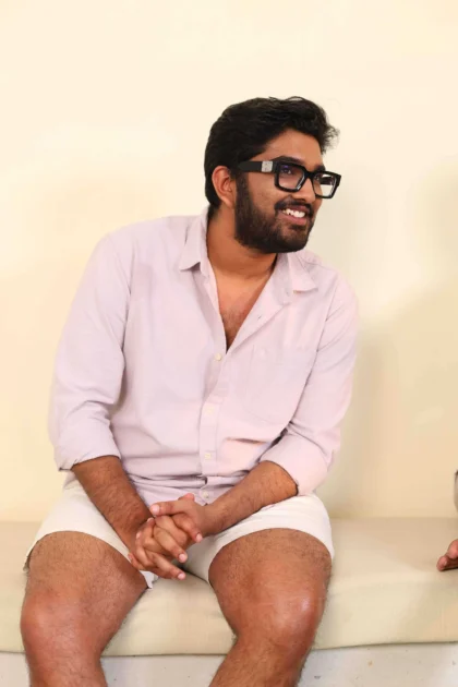 Man in light pink shirt smiling, seated with hands behind him.