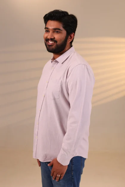 Smiling man in lavender shirt under warm light.
