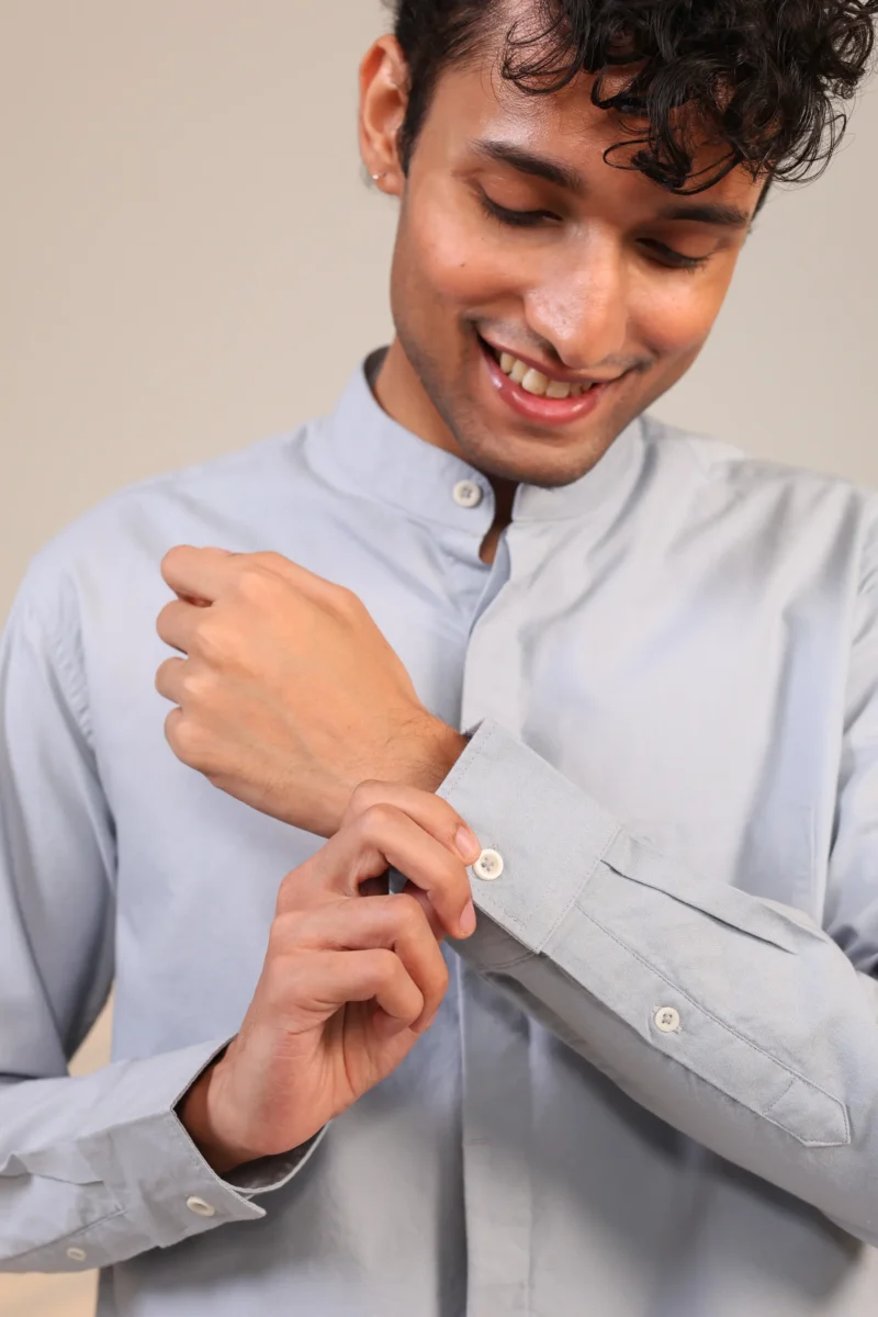Man adjusting cuff of light blue mandarin collar shirt.
