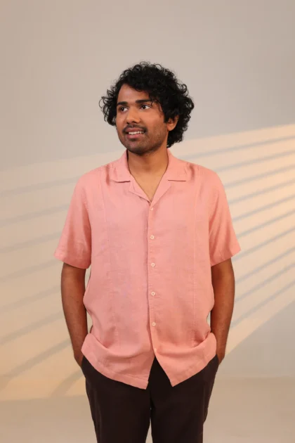Man smiling in short-sleeve coral shirt with hands in pockets. Rear view of light cream shirt with swirl pattern on back. Close-up of cream shirt with pocket and collar detail. Side view of cream shirt collar and chest area. Man buttoning cuff of light beige shirt.