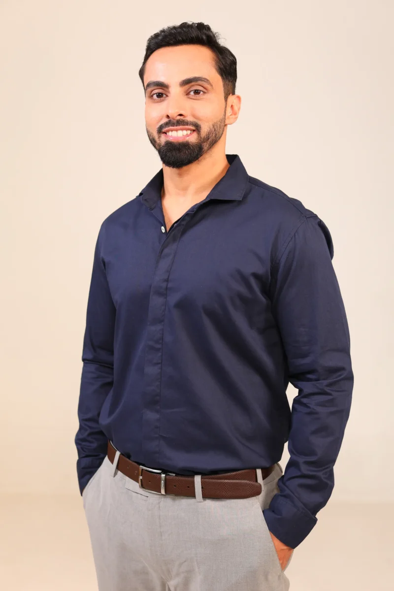 Man in dark navy shirt with sleeves down standing straight.