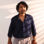 Man in navy blue shirt and grey pants standing in light.