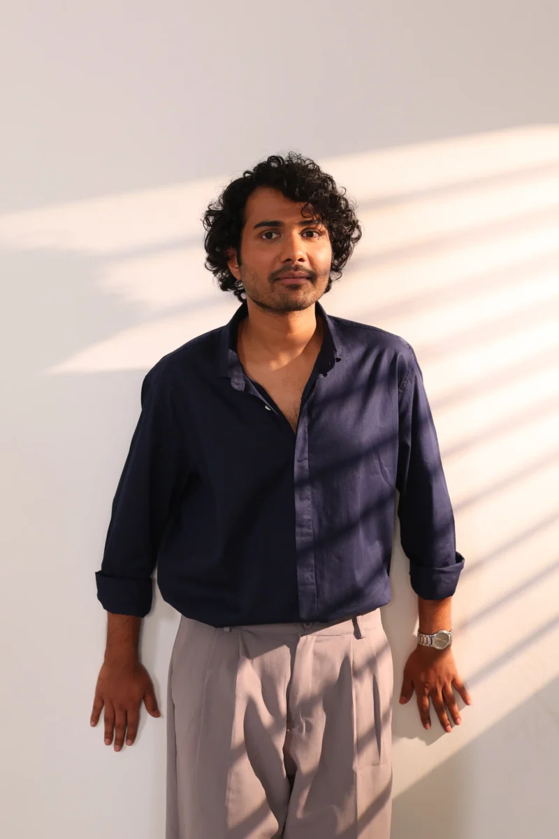 Man in navy blue shirt and grey pants standing in light.