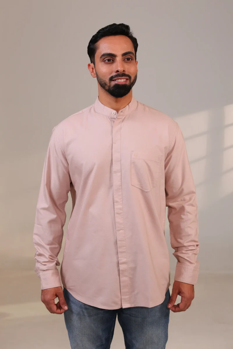 Man in pink shirt with sleeves down, standing in soft lighting