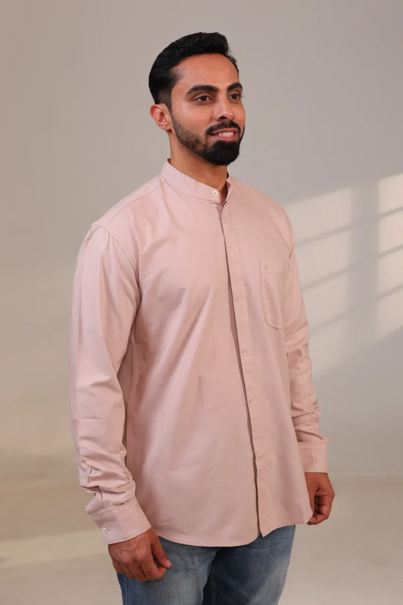 Man in pink mandarin collar shirt standing straight.