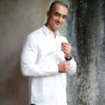 Man in a crisp white shirt adjusting his cuff indoors.