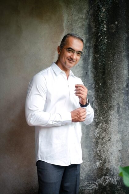 Man in a crisp white shirt adjusting his cuff indoors.